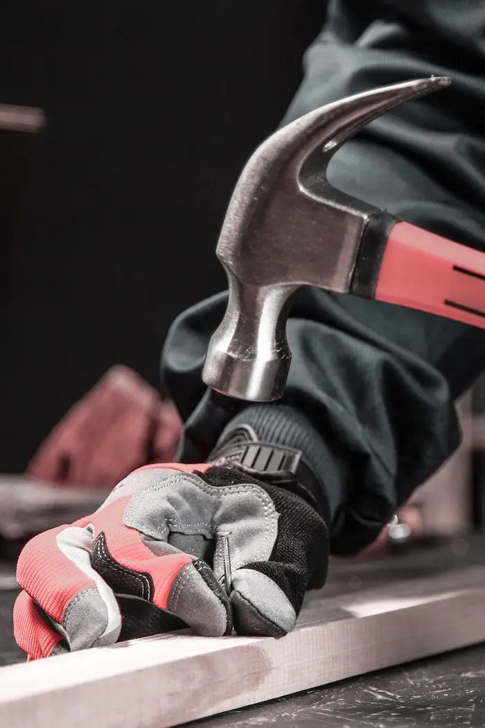 Ein Handwerker haut ein Nagel in eine Holzlatte