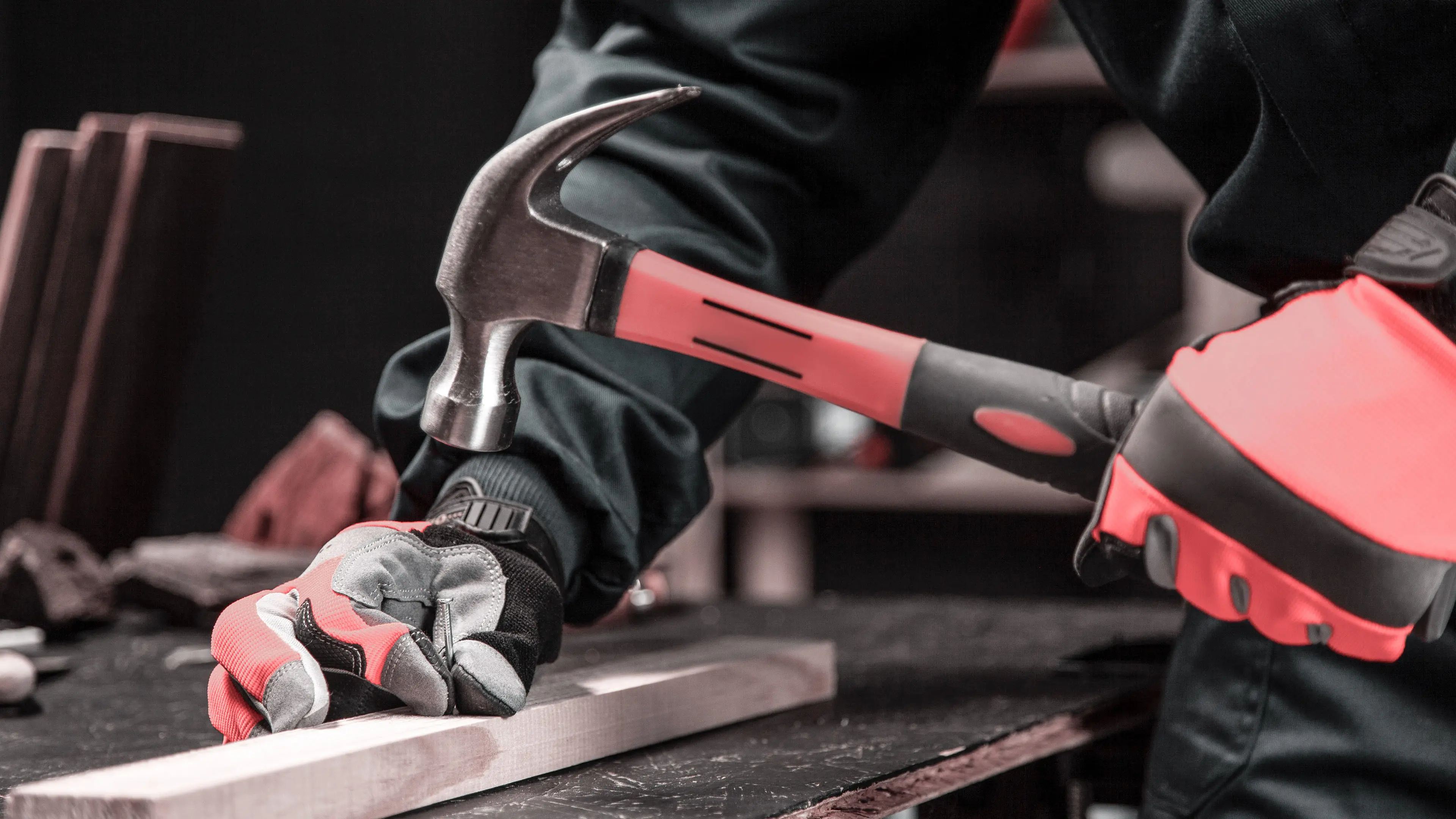 Ein Handwerker haut ein Nagel in eine Holzlatte